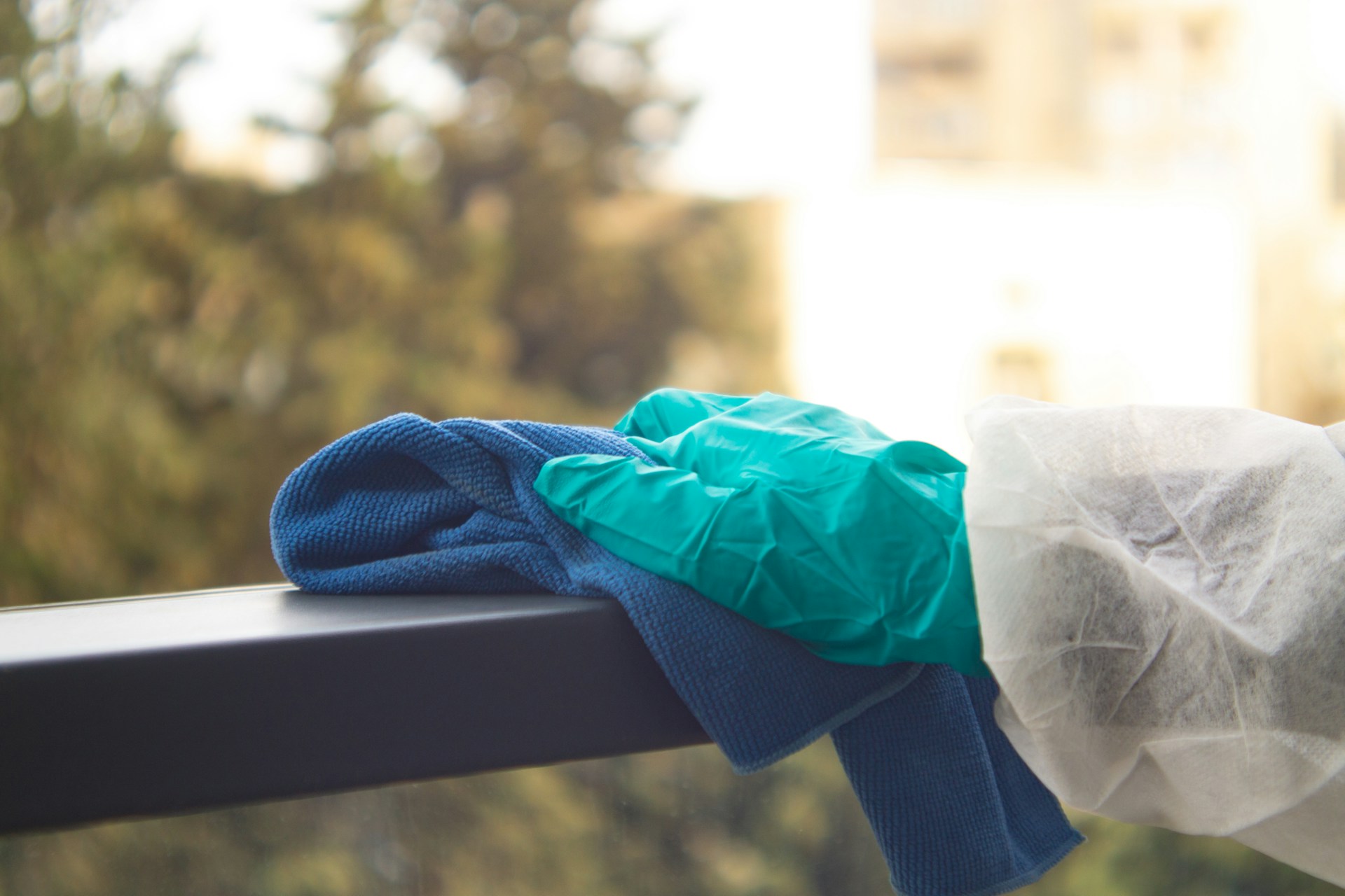 A close-up of a cleaner's hand polishing an outdoor banister with green cleaning products