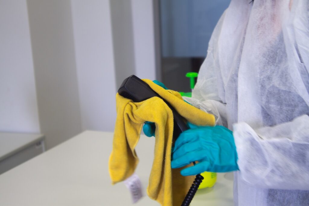 An office cleaner wiping down a landline phone with a yellow duster